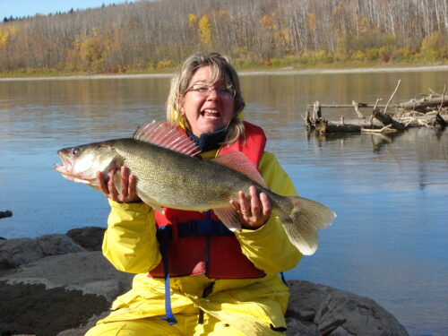 a woman in fishing gear holds up a big fish